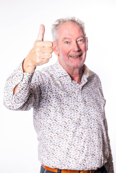 This image features a joyful senior man giving a thumbs up to the viewer, his face alight with a beaming smile. His enthusiastic gesture and cheerful demeanor suggest approval, success, or a positive - Photo, Image