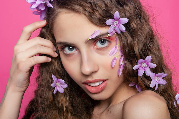 Natural beauty: Adorned with purple blooms, the girl's curly hair creates a captivating and enchanting sight, embodying floral allure - Фото, изображение