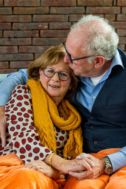 Esta cálida fotografía captura a una pareja de ancianos compartiendo un momento tierno. El hombre se inclina a susurrar afectuosamente a su pareja, que escucha con una sonrisa suave y contenta. Las mujeres. - Foto, imagen