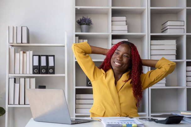 Femme d'affaires afro-américaine assise heureuse de faire du travail comptable et financier sur son bureau dans le bureau.. - Photo, image