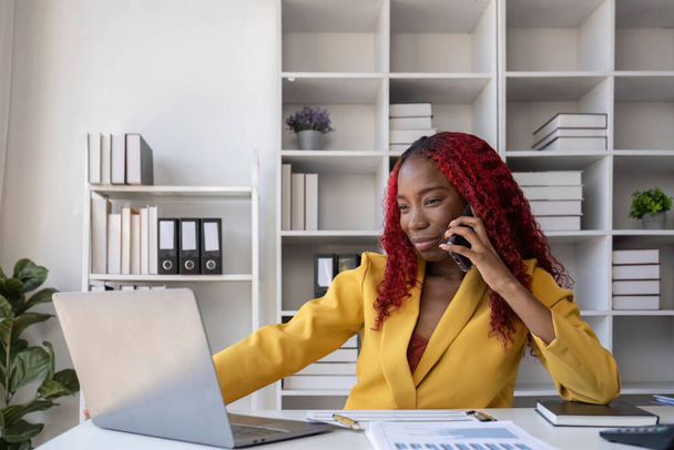 Fiatal afro-amerikai üzletasszony beszél telefonon és jegyzetel, miközben az irodában dolgozik.. - Fotó, kép