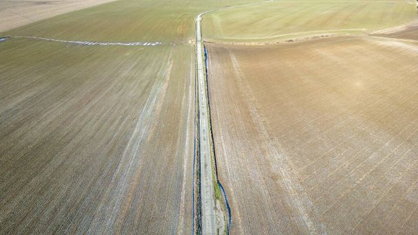Bu görüntü, iki farklı tarımsal alanı ikiye bölen kırsal yolun çarpıcı bir hava görüntüsünü yakalıyor. Soldaki alan, son hasat zamanının kalıntılarını gösteriyor. Toprakları bomboş. - Fotoğraf, Görsel