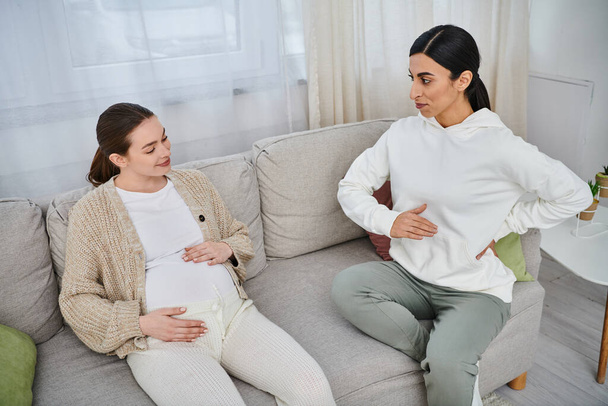 Eine schwangere Frau sitzt bei Elternkursen auf einer Couch neben ihrem Trainer und spiegelt sich gegenseitig. - Foto, Bild