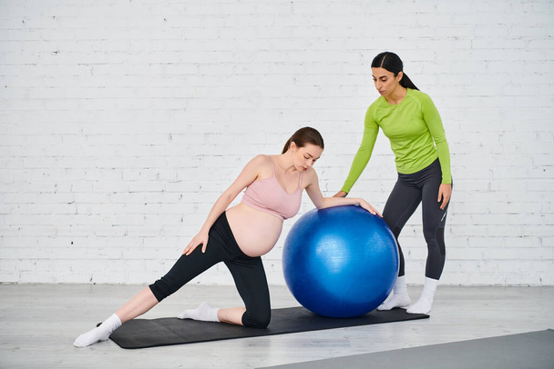 Egy terhes nő és az edzője a szülői tanfolyamok alatt jógagolyón gyakorlatoznak, elősegítve a fitnessz és wellness tevékenységet.. - Fotó, kép