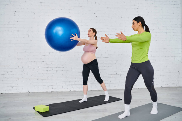 Μια έγκυος γυναίκα και ο προπονητής της κάνουν ασκήσεις με μια μπάλα κατά τη διάρκεια των μαθημάτων γονέων. - Φωτογραφία, εικόνα