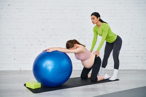 Eine schwangere Frau macht mit ihrem Trainer während eines Elternkurses Übungen auf einem Gymnastikball. - Foto, Bild