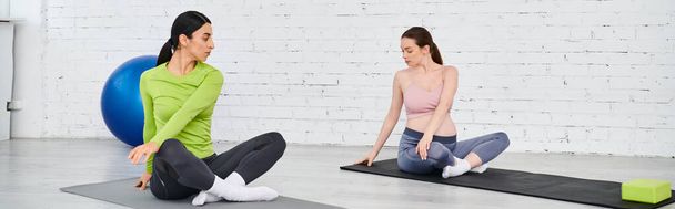 Dos mujeres, una embarazada, se sientan serenamente en colchonetas de yoga en un momento compartido de relajación y camaradería durante un curso para padres. - Foto, imagen