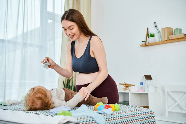 Una madre joven en una parte superior del sujetador juega alegremente con su bebé, curso de los padres en casa. - Foto, imagen