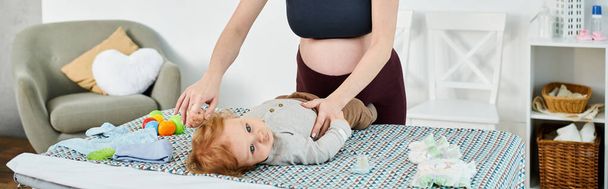 Una joven madre está de pie sobre su bebé acostado en una cama, durante un momento de crianza en casa. - Foto, Imagen