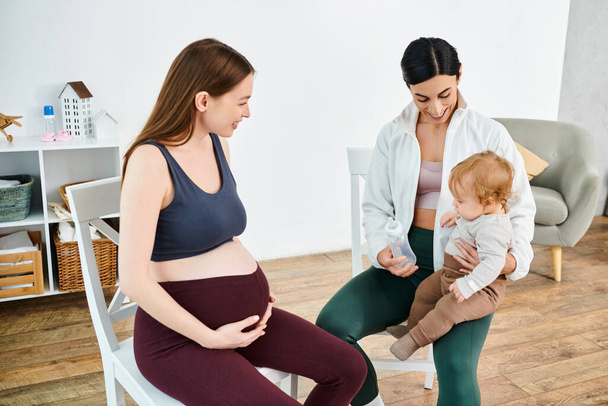 Egy terhes nő kecsesen ül egy széken, ölében ringatva egy babát az edzője támogatásával a szülői tanfolyamokon.. - Fotó, kép