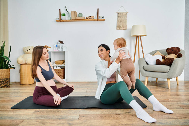 A young beautiful mother sits on a yoga mat, holding her baby in a calm and loving manner, guided by her coach at parents courses. - Photo, Image