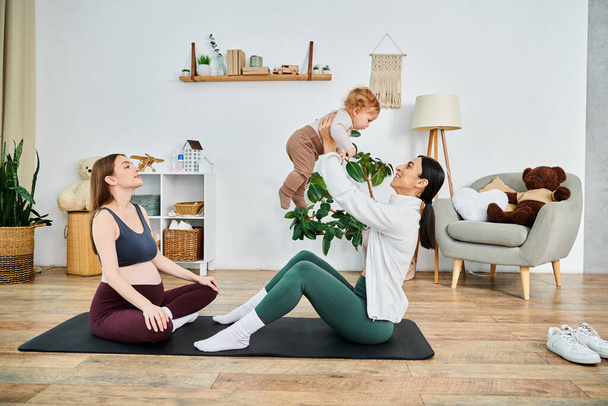 Eine junge Mutter sitzt friedlich auf einer Yogamatte, ihr Kind sitzt freudig auf ihren Schultern, angeleitet von einem unterstützenden Trainer. - Foto, Bild