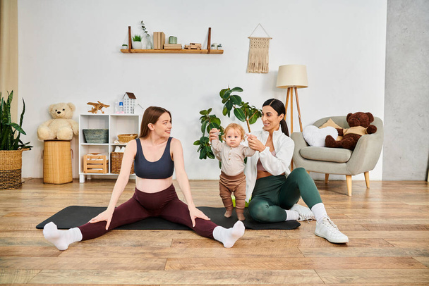 Eine junge schöne Mutter sitzt auf einer Yogamatte und wiegt ihr Baby unter Anleitung ihres Trainers bei Elternkursen. - Foto, Bild