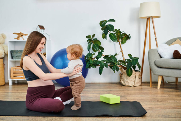 Uma bela jovem mãe sentada em um tapete de ioga, embalando seu bebê com a orientação de um treinador em cursos de pais. - Foto, Imagem