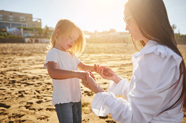 Mam en dochter spelen op het strand, houden elkaars hand vast en brengen gelukkige momenten samen door. Familie relaties. Zwangerschaps- en opvoedingsconcept - Foto, afbeelding