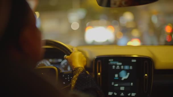 Weibliche Person mit schwarzen gelockten Haaren am Steuer eines Autos in der Stadt bei Nachtampeln. Hochwertiges 4k Filmmaterial - Filmmaterial, Video