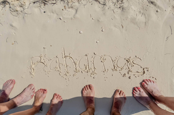 Escape caribeño de amigos: Los turistas escriben 'Bahamas' en la arena, los dedos de los pies inmersos, capturando momentos soleados en su idílico retiro en la playa - Foto, imagen