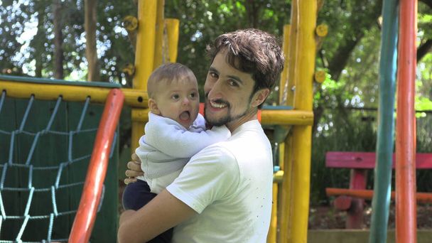 カメラ本物のカジュアルな笑顔と関係を探している赤ちゃんの息子を抱えている父親 - 写真・画像