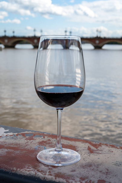 Γευσιγνωσία του Bordeaux αναμιγνύονται κόκκινο κρασί με την πόλη του κρασιού Μπορντό στο παρασκήνιο, αριστερά όχθη της εκβολής Gironde, Γαλλία. Ποτήρι κόκκινο γαλλικό κρασί σερβίρεται εξωτερική. - Φωτογραφία, εικόνα