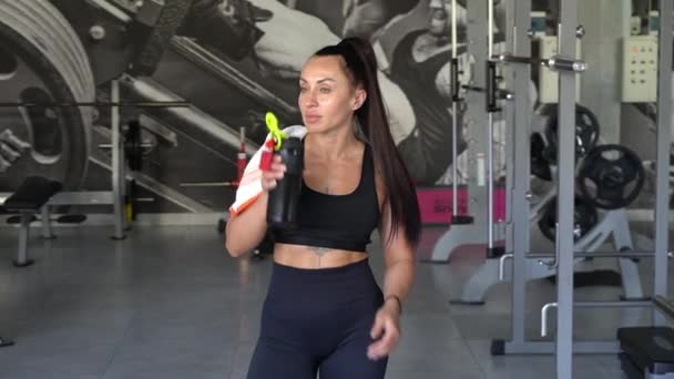 Portrait of a woman with a beautiful figure in the gym. Woman in workout clothes drinking water in the gym. A break between training sessions - Footage, Video