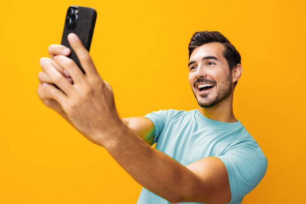 Мужчина студийное сообщение портрет улыбающийся смартфон очки стиль жизни коммуникация удивить бизнес-копирования технологии киберпространства мобильного указывая счастливый телефон пространство телефона желтый - Фото, изображение