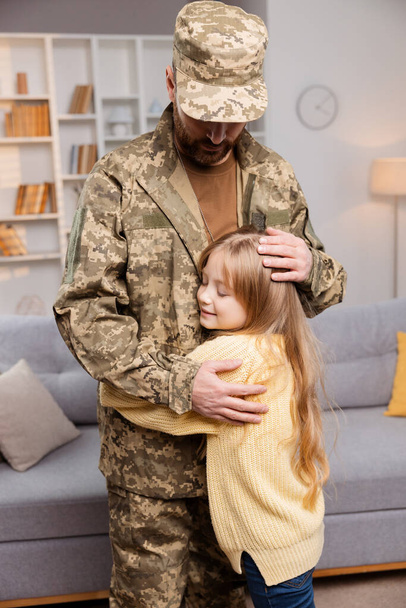 軍服を着た父親が ジョイスの娘の周りに腕を振り回し 自宅の暖かさに立った 兵士の故郷の心からの光景が広がります。 兵士は愛する人たちと再会する瞬間を大切にしています - 写真・画像