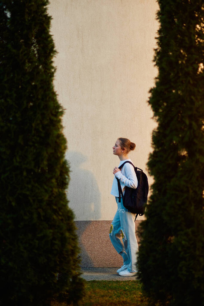 Una bella adolescente europea, catturata in un ritratto di profilo laterale, torna a casa al tramonto dopo la scuola, portando lo zaino. - Foto, immagini