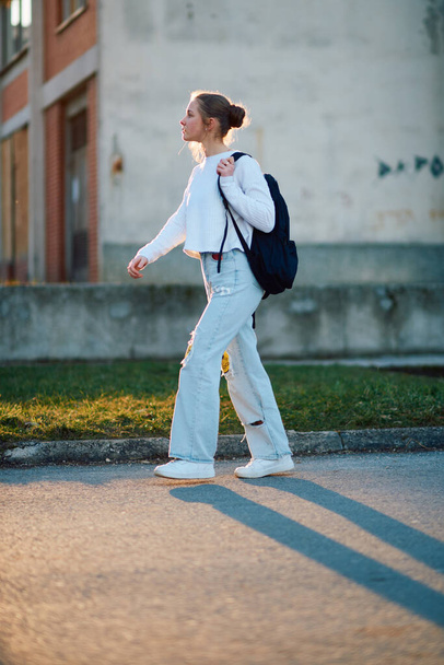 Egy gyönyörű európai tinédzser, egy oldalsó profilképpel, hazafelé sétál napnyugta után iskola után, a hátizsákját cipelve.. - Fotó, kép