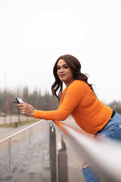 Trans mulher usando tablet digital e inclinando-se sobre trilhos. Ela está sorrindo para o espectador. Foto de alta qualidade - Foto, Imagem