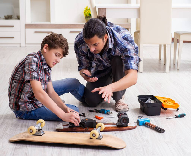 若い父親は息子とスケートボードを家で修理する - 写真・画像
