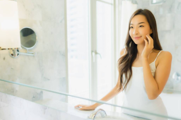 Portret piękna młoda azjatycka kobieta sprawdzić i makijaż jej twarz na lustrze we wnętrzu łazienki - Zdjęcie, obraz