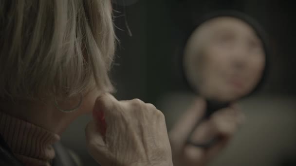 Oude vrouw die zichzelf in spiegelbeeld bekijkt denkend aan het verleden - Video