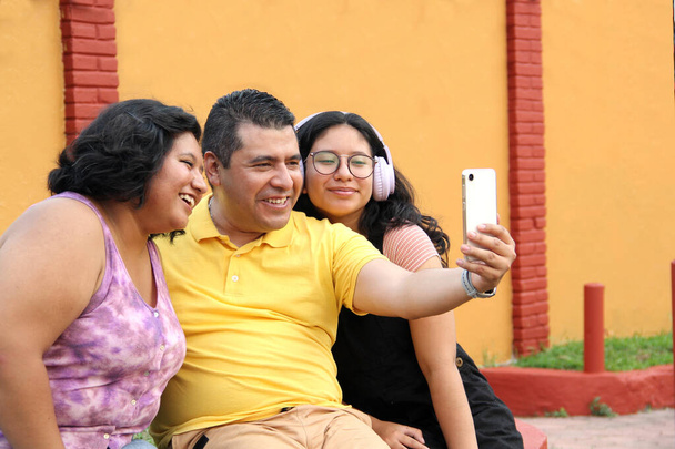 Rozwiedziony samotny ojciec ze swoimi ciemnoskórymi latynoskimi córkami spędza miło czas korzystając z telefonu komórkowego robiąc zdjęcia selfie - Zdjęcie, obraz