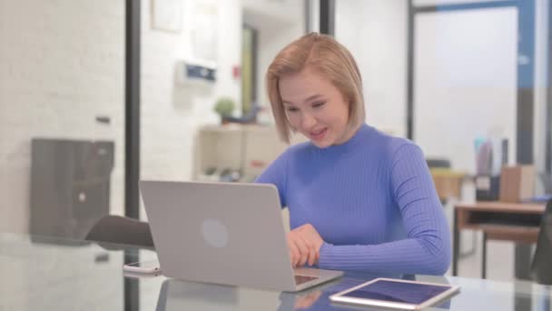 Νεαρή γυναίκα συνομιλεί στο διαδίκτυο στο φορητό υπολογιστή, ενώ κάθεται στο γραφείο - Πλάνα, βίντεο