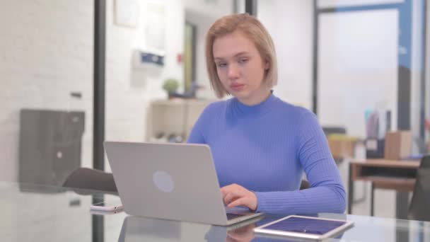 Молодая женщина смотрит в камеру во время работы над ноутбуком в офисе - Кадры, видео