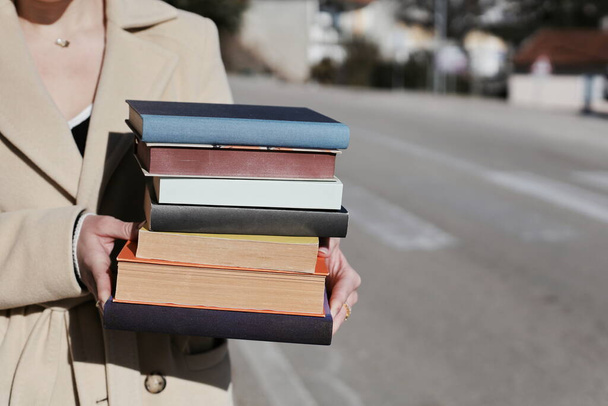 στοίβα από βιβλία στα χέρια μιας γυναίκας σε ένα γκρι φόντο τοίχο από τούβλα - Φωτογραφία, εικόνα