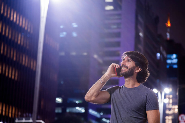 Fiatal férfi használ okostelefon éjjel a városra néző táj és az autó forgalom a háttérben.  - Fotó, kép
