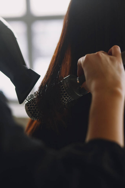 Майстер жінка перукар сушить волосся дівчини феном і гребінцями після миття в салоні краси - Фото, зображення