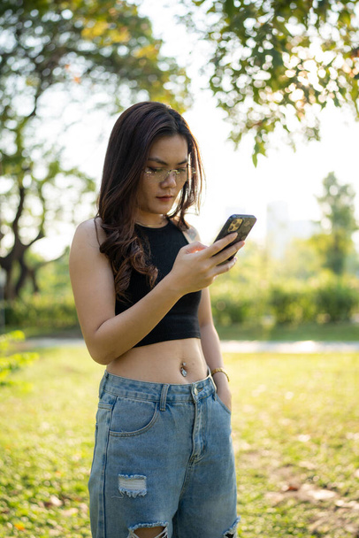Business casual asian woman use smartphone in city park sunset light online business communication - Foto, Bild