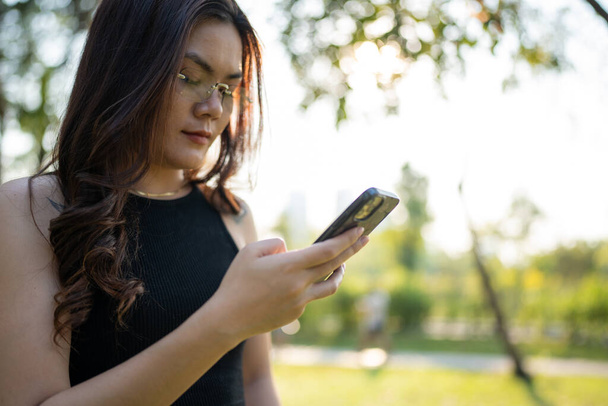 Business casual asian woman use smartphone in city park sunset light online business communication - Foto, Bild