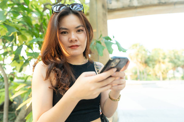 Ділова випадкова азіатка використовує смартфон у міському парку захід сонця світло онлайн ділове спілкування - Фото, зображення