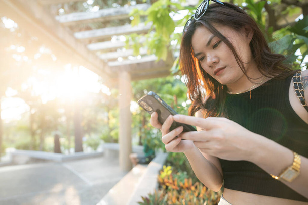 Ділова випадкова азіатка використовує смартфон у міському парку захід сонця світло онлайн ділове спілкування - Фото, зображення