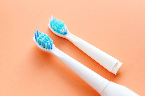 Primer plano de dos cepillos de dientes blancos con cerdas azules, uno nuevo y el otro usado y utilizado sobre un fondo naranja. - Foto, imagen