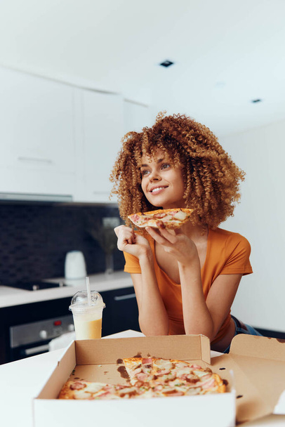 A woman with curly hair enjoying a slice of pizza while sitting at a table - Photo, Image