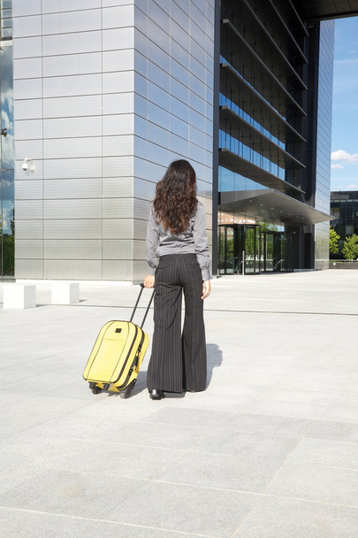 Бізнес-леді з жовтою валізою перед бізнес-будівлею
 - Фото, зображення