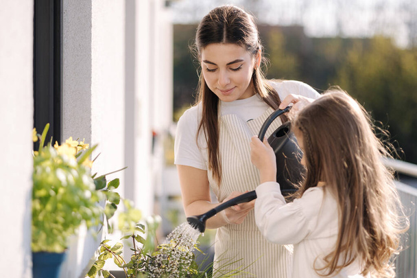 Máma zalévá kytku se svou roztomilou dceruškou. Šťastné rodinné zahradničení na balkóně. Kvalitní fotografie - Fotografie, Obrázek