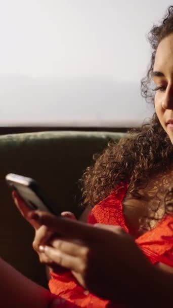 Menina morena mensagens de texto em seu telefone celular por uma janela ensolarada - FHD Vertical vídeo - Filmagem, Vídeo