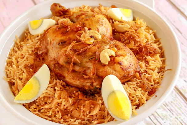 Saúdské kuřecí Kabsa pulao rýže se smaženou cibulí, kešu oříškem a vařeným vejcem podávané v hrnci izolované na dřevěném stole pohled na arabské kořeněné jídlo - Fotografie, Obrázek