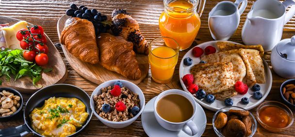 Breakfast served with coffee, orange juice, scrambled eggs, cereals, pancakes and croissants. - Photo, image