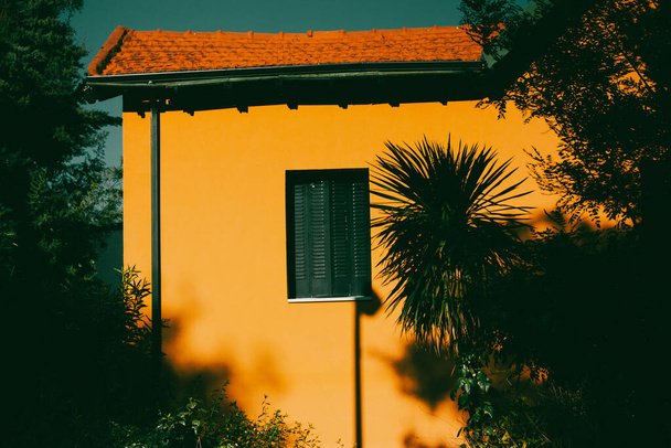Güneşli bir günde yeşil panjurlu turuncu bina. Palmiye ağaçlarının arasında kırsal bir ev. Villa, kulübe, yaz tatili için dağ evi. Yazlık ev - Fotoğraf, Görsel